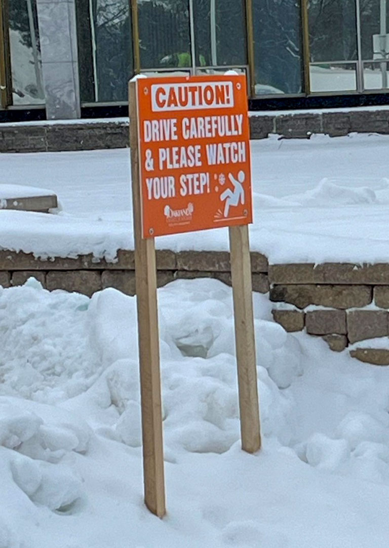 A caution sign reminding drivers to drive carefully and urging pedestrians to watch their steps for safety.