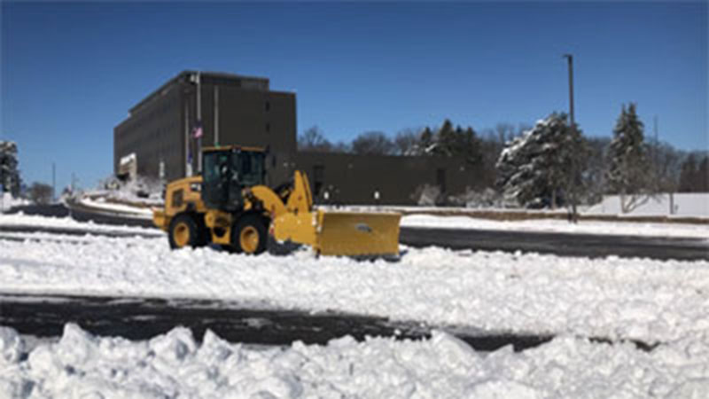 Snowplow truck shoveling snow in a county building parking lot.
