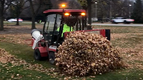 A man driving a tractor through the park with leaves.