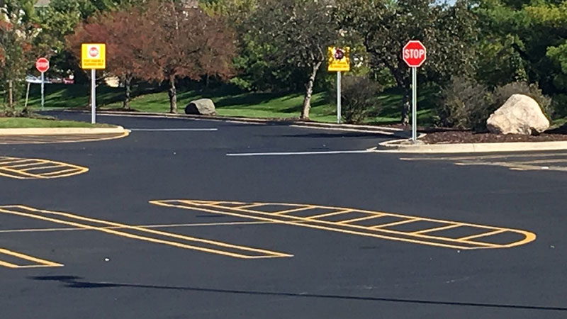 A freshly paved and empty parking lot with multiple stop signs, signs, and lane markings.