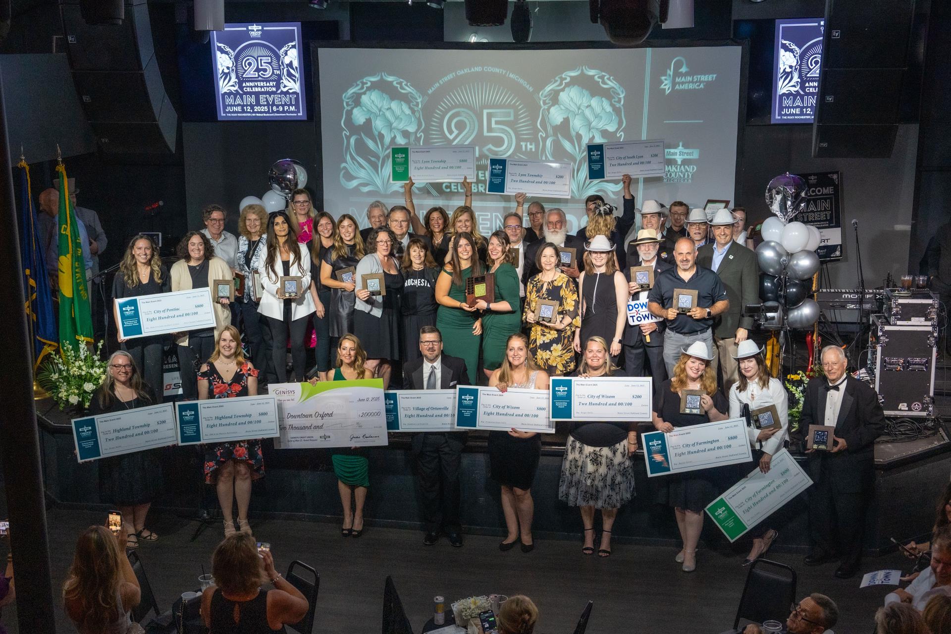 A large group of people stand on a stage holding awards