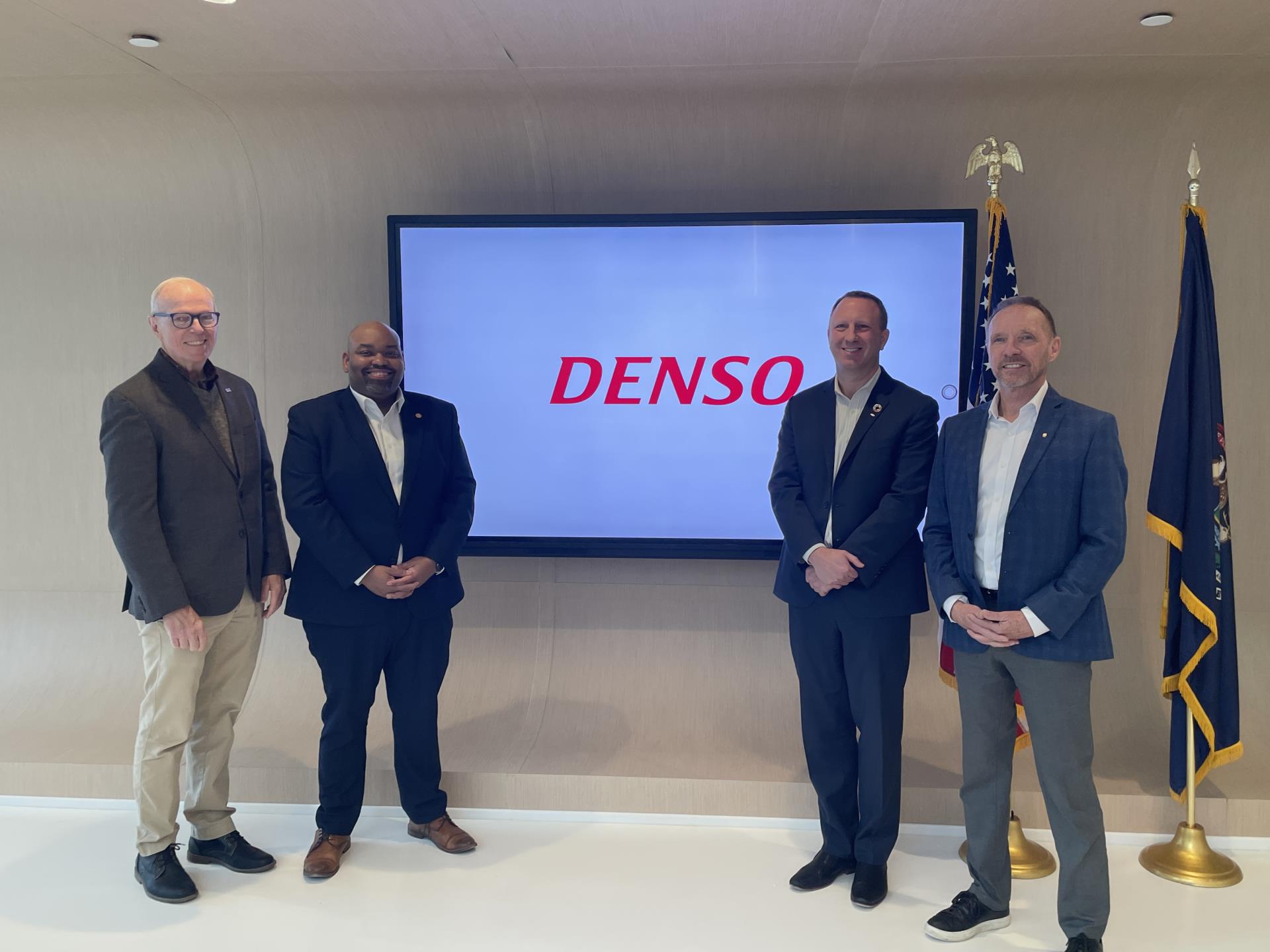 Four men stand in front of TV with DENSO logo